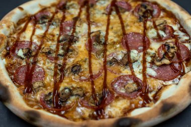 freshly made pizza close-up; details of the pizza application; juicy pizza from the oven with mushrooms, tomatoes and bacon and sprinkled with parmesan cheese