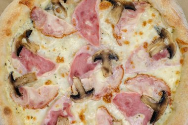 freshly made pizza close-up; details of the pizza application; juicy pizza from the oven with mushrooms, tomatoes and bacon and sprinkled with parmesan cheese