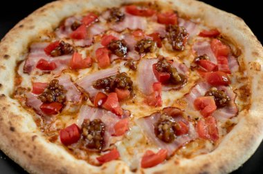 freshly made pizza close-up; details of the pizza application; juicy pizza from the oven with mushrooms, tomatoes and bacon and sprinkled with parmesan cheese