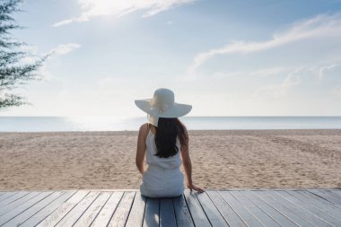 Yaz tatilinde sahilde, deniz manzarasının tadını çıkaran genç bir kadın.