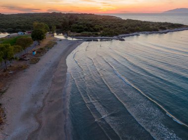 Yumuşak dalgaları ve ormanlık adası olan günbatımı kumsalı