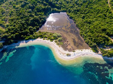 Turkuaz suları ve yemyeşil suları olan tenha bir sahil koyunun havadan görünüşü..
