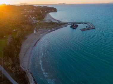 Küçük bir limanı olan pitoresk bir sahil şeridinin günbatımı görüntüsü.