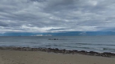 Sakin deniz manzarası, bulutlu bir gökyüzünün altında uzak dağlar. Roda Plajı, Korfu, Yunanistan 