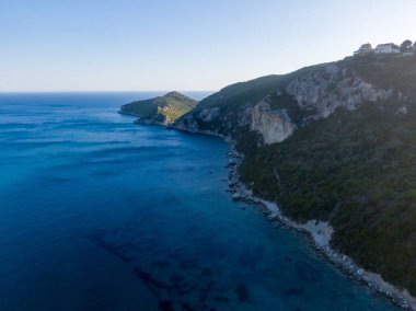 Derin mavi suları ve engebeli bir uçurumu olan sakin bir kıyı şeridi..
