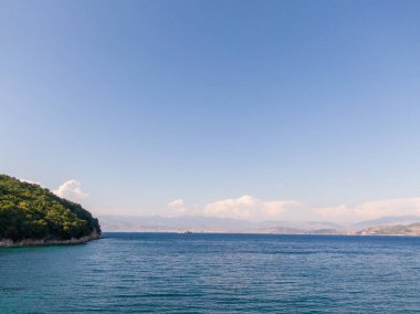 Berrak gökyüzünün altında yemyeşil bir adası olan sakin mavi deniz manzarası.
