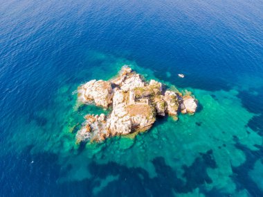 Uçsuz bucaksız mavi denizde harap olmuş küçük, kayalık bir adanın havadan görünüşü..