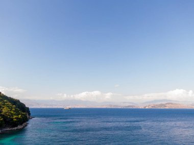 Berrak mavi gökyüzünün altında turkuaz suları ve uzak adaları olan sakin deniz manzarası.