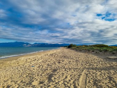 Dağları ve bulutlu gökyüzü ile sakin kumlu sahil.