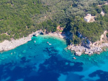 Turkuaz su, tekne ve yemyeşil ormanlı tenha bir koy manzarası..