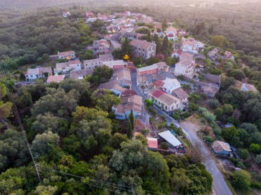 Bereketli yeşilliğin ortasında, gün batımının yumuşak parıltısıyla yıkanmış sakin bir köyün havadan görünüşü..