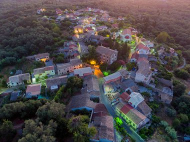 Alacakaranlıkta ağaçların arasına kurulmuş küçük bir köyün havadan görünüşü.