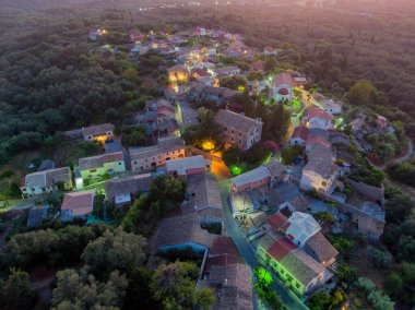 Alacakaranlıkta yemyeşil yemyeşil ortamda yuva yapmış sakin bir köyün havadan görünüşü.