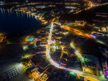 Kıyı kasabası gece aydınlandı. Binaların, sokakların ve kıyı şeridinin havadan görüntüsü.