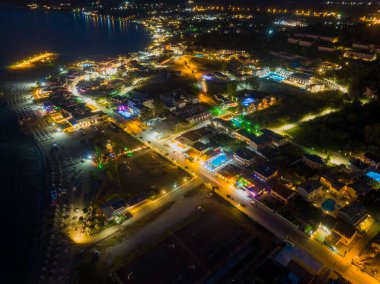 Aydınlatılmış sokakları, binaları ve plajı olan kıyı kasabasının gece görüşü..