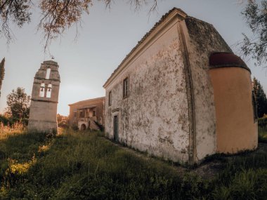 Eski, yıpranmış bina ve gün batımında çan kulesi.