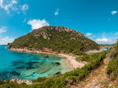 Turkuaz suyu olan tenha bir sahil ve mavi gökyüzünün altında yemyeşil bir dağ..