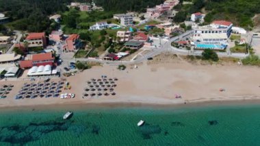 Kumlu bir sahil ve tatil köyü yakınında yelkenli ve rüzgar sörfçüleriyle turkuaz bir okyanusun havadan görünüşü. Korfu, Yunanca