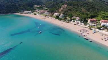Kumlu bir sahil ve tatil köyü yakınında yelkenli ve rüzgar sörfçüleriyle turkuaz bir okyanusun havadan görünüşü. Korfu, Yunanca