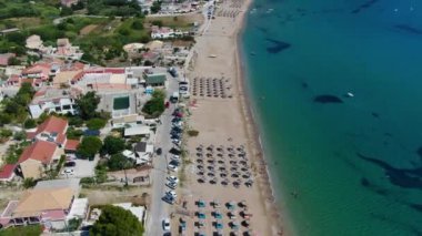 Kumlu bir sahil ve tatil köyü yakınında yelkenli ve rüzgar sörfçüleriyle turkuaz bir okyanusun havadan görünüşü. Korfu, Yunanca