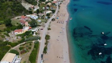 Kumlu bir sahil ve tatil köyü yakınında yelkenli ve rüzgar sörfçüleriyle turkuaz bir okyanusun havadan görünüşü. Korfu, Yunanca