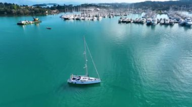 Mavi gökyüzünün altında turkuaz sularda marina yakınlarında yelkenli.