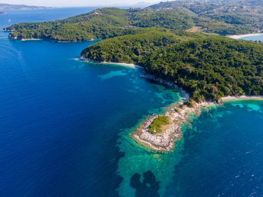 Berrak turkuaz suları olan, yemyeşil bitki örtüsü ve kayalık kıyılarla çevrili tenha bir körfezin havadan görünüşü..