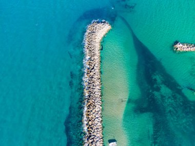 Canlı bir turkuaz denize uzanan taştan bir dalgakıranın havadan görünüşü. Temiz su kumlu deniz yatağını ortaya çıkarıyor..