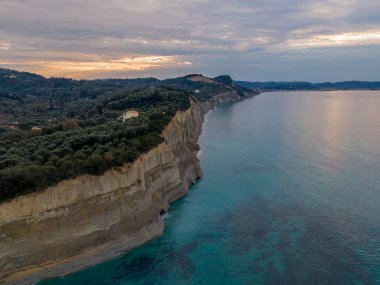 Coastal cliffs and turquoise sea at sunset. Serene landscape with lush greenery atop the cliffs. clipart