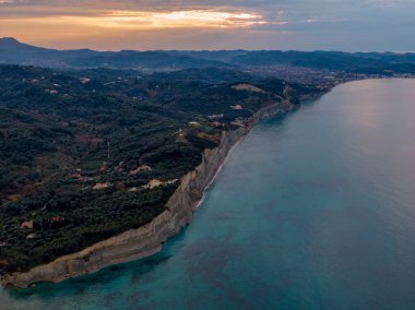 Gün batımında kıyı kayalıkları, sakin okyanusa ve uzak tepelere bakıyor..