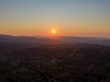 Yuvarlanan tepelerin ve vadilerin üzerinde gün batımı, arazide sıcak altın bir ışık yayıyor. Huzurlu ve huzurlu bir sahne.