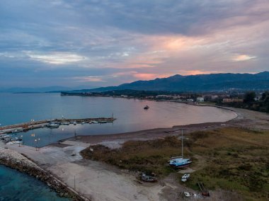 Gün batımında sahil kasabası, limandaki tekneler, gökyüzünün renklerini yansıtan sakin sular..