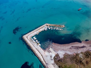 Taştan bir rıhtım boyunca yanaşmış küçük bir limanın havadan görüntüsü, açık turkuaz bir su zeminine karşı kurulmuş..