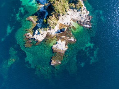 Kayalık kıyı şeridi ve berrak turkuaz suyu olan küçük bir adanın havadan görüntüsü..