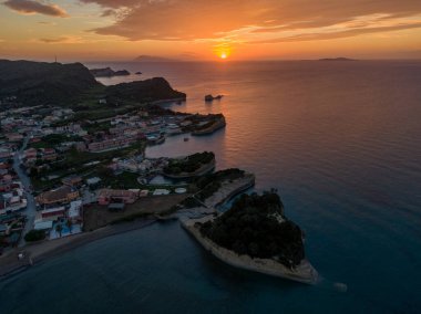 Sahil kasabasında ve okyanusta gün batımı. Altın saat ışığı sahneyi yıkıyor, binaları ve dramatik uçurumları aydınlatıyor..