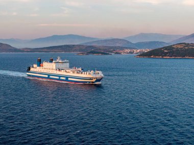 Feribot gün batımında dağların yakınında sakin bir denizde yol alıyor..