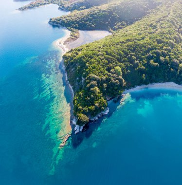 Bereketli yeşil bir yarımadanın turkuaz okyanus sularıyla buluşmasının havadan görüntüsü. Kristal berrak sığlıklar koyu mavi ile buluşur.
