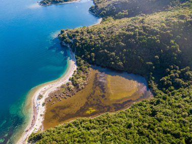 Bereketli yeşillik ve canlı mavi deniz arasında kurulmuş sakin bir lagün ile tenha bir koyun havadan görünüşü..
