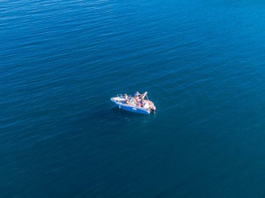 İçinde insanların olduğu küçük bir motorlu tekne sakin ve derin bir mavi denizde yüzüyor. Hava görünümü.