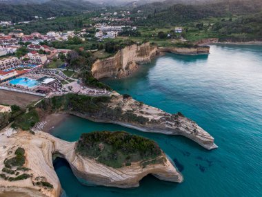 Benzersiz kaya oluşumları ve turkuaz sularıyla çarpıcı bir kıyı manzarası. Tepenin yamacına yerleşmiş bir tatil köyü var..