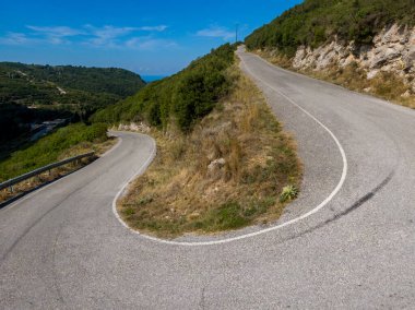 Manzaralı tepelerin arasından dolambaçlı bir yol ve parlak mavi gökyüzünün altında yemyeşil bir yer. Doğanın güzelliğinde bir yolculuk.