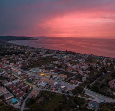 Gün batımında sahil kasabası, hava manzaralı. Sakin denizin ve evlerin üzerinde pembe gökyüzü.