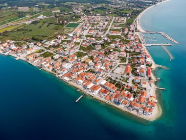 Sahil kasabasının hava manzarası. Binalar kıyı şeridi boyunca uzanır, berrak mavi sularla buluşurlar. Küçük bir liman görünüyor..