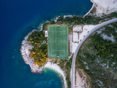 Sahil futbol sahası hava manzarası. Yeşil alan kayalık bir yarımadada, yol ve okyanusun yanında. Drone fotoğrafçılığı.