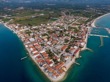 Sahil kasabasının hava manzarası. Kırmızı çatılı binalar turkuaz su, pitoresk bir liman ve yeşil manzarayla çevrilidir..