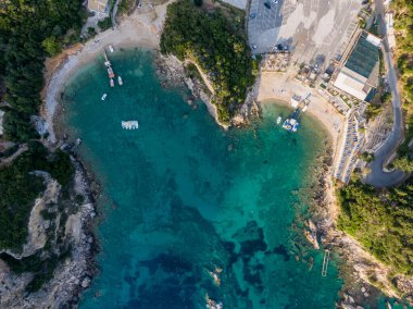Tenha bir koy, turkuaz su, tekne ve küçük bir plaj manzarası..