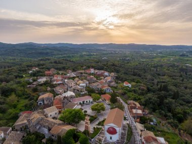 Tepelerle çevrili yemyeşil bir vadiye kurulmuş büyüleyici bir köyün gün batımı manzarası..