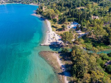 Çarpıcı bir sahil manzarası, kristal berraklığında turkuaz su, yemyeşil ve kıyıya yakın küçük bir bina..