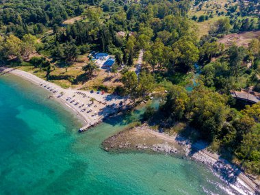 Turkuaz suyu, yemyeşil yeşillik ve yakınındaki küçük bir binanın bulunduğu tenha bir sahil manzarası..