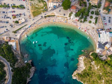 Kristal berraklığında turkuaz su, kumlu bir sahil ve çevresindeki binalarla gözlerden uzak bir koy manzarası..